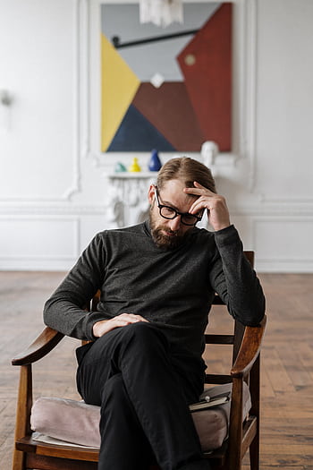 A man sits pensively in a chair, surrounded by abstract art in a stylish room. HD phone wallpaper