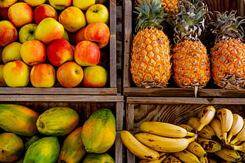 Colorful display of apples, pineapples, bananas, and papayas in wooden crates at a market. HD wallpaper