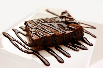 Rich chocolate brownie drizzled with syrup on a clean white plate, perfect for dessert lovers. HD wallpaper