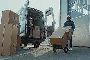 Two couriers load boxes into a van for shipment, showcasing logistics and teamwork. HD wallpaper