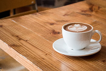 Close-up of a white cup of latte with artistic foam on a rustic wooden table. HD wallpaper