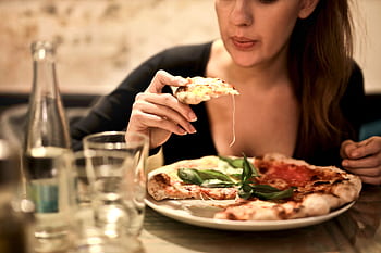 A woman savoring a delicious pizza slice in a cozy indoor restaurant setting. HD wallpaper