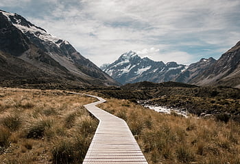 Wooden walkway leads through rugged landscape towards majestic snow-capped mountains. HD wallpaper