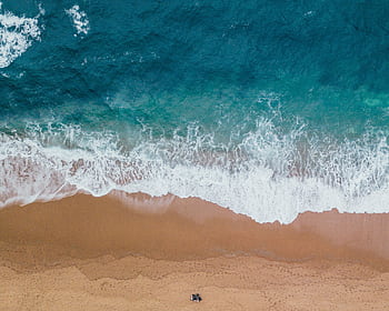 A stunning aerial shot capturing waves gently crashing onto a sandy beach, showcasing the beauty of the ocean. HD wallpaper