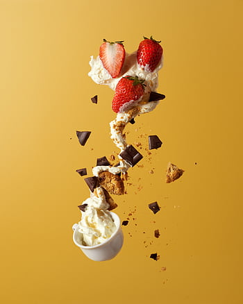 Delicious strawberries and cream with chocolate and cookie pieces, captured in mid-air against a vibrant yellow background. HD phone wallpaper