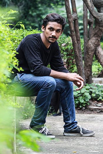 Young male model in casual attire sitting in a green park, showcasing relaxed lifestyle outdoors. HD phone wallpaper