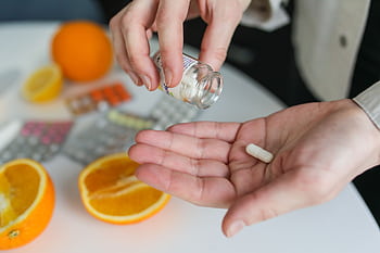 Close-up of a person taking a vitamin capsule with citrus fruit and medication on a table. HD wallpaper