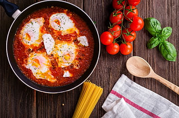 Delicious eggs in tomato sauce with basil, spaghetti, and fresh tomatoes on a wooden table. HD wallpaper