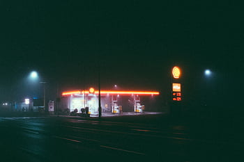 A foggy night scene of an illuminated gas station, featuring vibrant neon lights. HD wallpaper