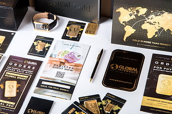 Flat lay of promotional materials for gold investment, featuring brochures, cards, and gold bars. HD wallpaper