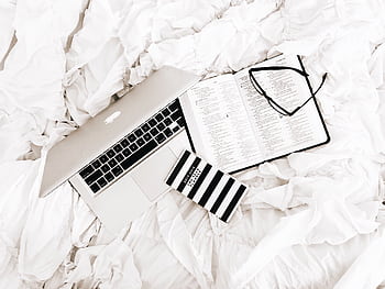 A flat lay of a laptop, open book, and reading glasses on a white bed. Perfect for productivity and relaxation themes. HD wallpaper