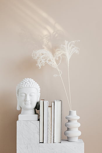 A minimalist decor setup featuring a Buddha head sculpture with books and a vase on a marble shelf. HD phone wallpaper