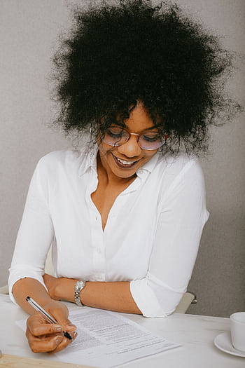 Smiling woman in business attire signing documents at a desk indoors. HD phone wallpaper
