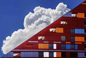 Colorful modern building facade against a backdrop of dramatic clouds and bright blue sky. HD wallpaper