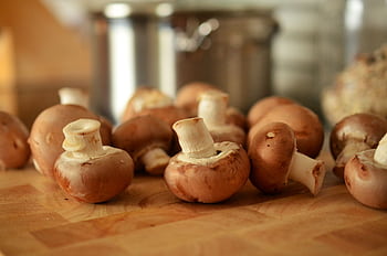 Close-up of fresh brown mushrooms on a wooden cutting board in a kitchen setting. HD wallpaper