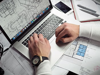 Architect reviewing detailed floor plans and schematics on a laptop with a smart nearby. HD wallpaper