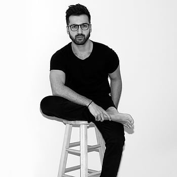 Black and white of a man sitting on a stool indoors, looking pensive and fashionable. HD phone wallpaper