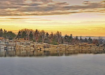 Rocky River View, yellow sky, evergreens, bare trees, grey clouds, water, rocks HD wallpaper