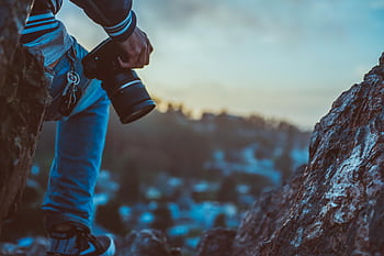 grapher with camera outdoors on rocks during sunset capturing the scenic view. HD wallpaper