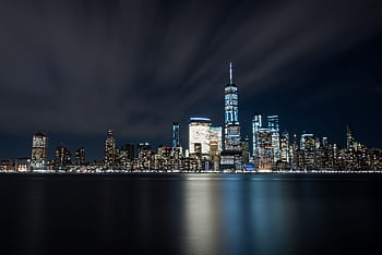 Illuminated New York City skyline featuring One World Trade Center reflecting in the river at night. HD wallpaper