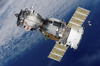 Close-up of Soyuz spacecraft orbiting Earth with solar panels extended, showcasing space exploration technology. HD wallpaper