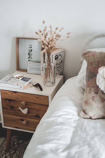 A cozy minimalist bedroom with a stylish nightstand featuring books and a vase of dried flowers. HD phone wallpaper