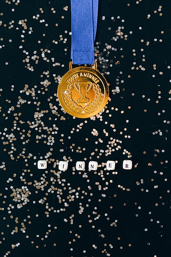 Gold medal on a black surface with confetti and 'winner' spelled out. HD phone wallpaper
