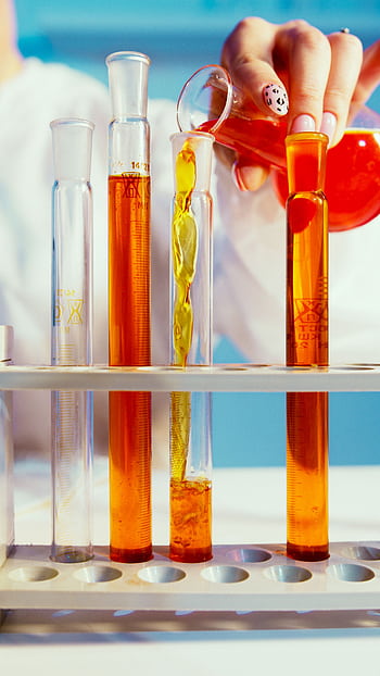 Close-up of a lab technician pouring orange liquid into test tubes in a laboratory setting. HD phone wallpaper