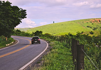 A car travels on a winding rural road in lush Brazilian countryside under a blue sky. HD wallpaper