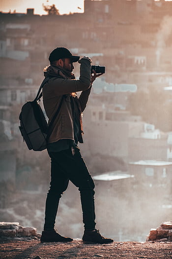 A grapher in a jacket capturing a city view with a DSLR during sunset. HD phone wallpaper