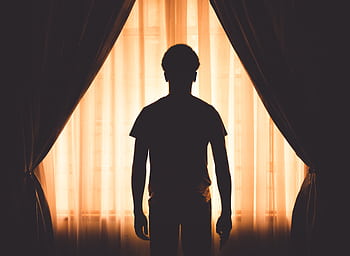 A silhouette of a man standing by a window with curtains, creating a dramatic contrast and mood. HD wallpaper