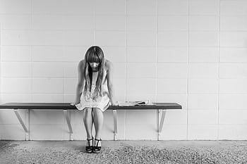 A black and white of a woman in thought, sitting on a bench indoors, portraying solitude. HD wallpaper