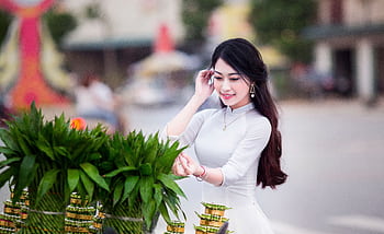 A smiling woman in a white dress near lush greenery outdoors, exuding joy. HD wallpaper