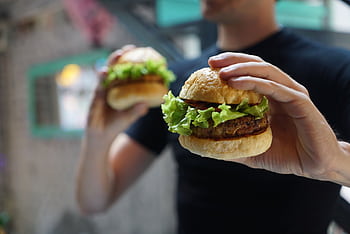 A close-up shot of a person holding a homemade burger with fresh lettuce, ideal for fast food themes. HD wallpaper