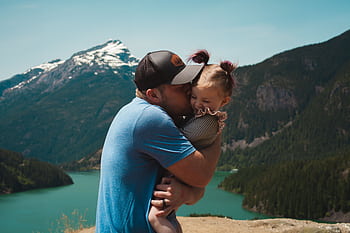 A heartwarming scene of a father hugging his daughter in a stunning mountain landscape. HD wallpaper