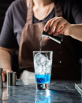 A bartender pouring a refreshing blue cocktail over ice in a glass. HD phone wallpaper