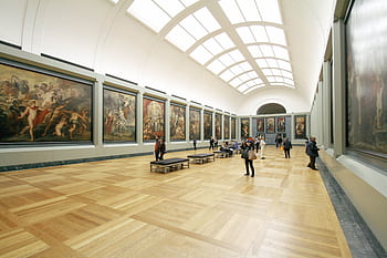 A wide view of a museum hall showcasing famous paintings and visitors exploring the art. HD wallpaper