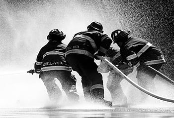 Firefighters in full gear battle heavy water spray in an intense operation. HD wallpaper