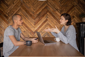 Two colleagues discussing a project over coffee in a modern, cozy workspace. HD wallpaper