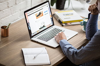Adult working on a laptop in a modern office setting, illustrating productivity and concentration. HD wallpaper