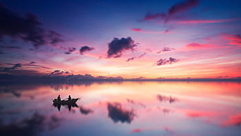 A tranquil sunset scene with a boat silhouetted against a vibrant sky reflected on a calm lake. HD wallpaper