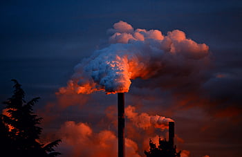 Smoke billows from industrial chimneys at sunset, highlighting pollution against a vibrant sky. HD wallpaper