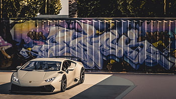 A sleek luxury sports car parked in front of a vibrant graffiti wall under bright daylight. HD wallpaper