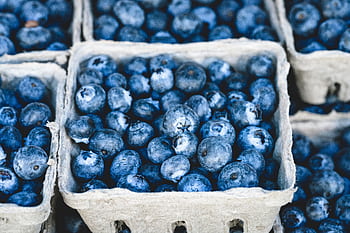 Close-up of fresh organic blueberries in cardboard trays at a market, showcasing their vibrant blue color and ripe appearance. HD wallpaper