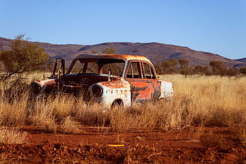 Vintage car decaying in a dry desert landscape with mountains in the background. HD wallpaper