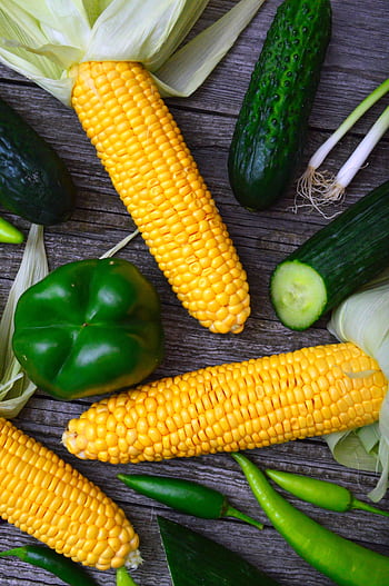 A vibrant assortment of fresh corn, peppers, and cucumbers on a wooden table. HD phone wallpaper