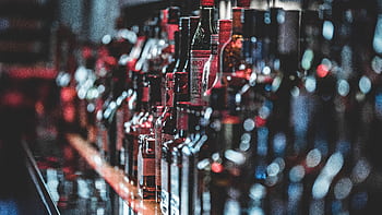 Blurred view of assorted alcohol bottles lined up on a bar shelf indoors. HD wallpaper