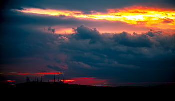 Captivating sunset casting vibrant colors over a silhouetted landscape and dramatic clouds. HD wallpaper