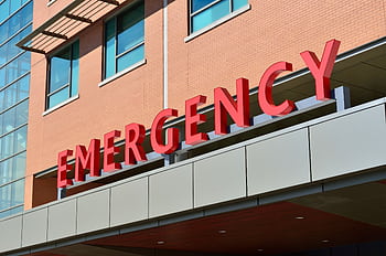 Close-up of a modern hospital emergency room entrance with prominent red letters. HD wallpaper