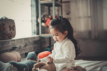 Adorable Asian child playing with stuffed toys indoors, showcasing innocent childhood moments. HD wallpaper